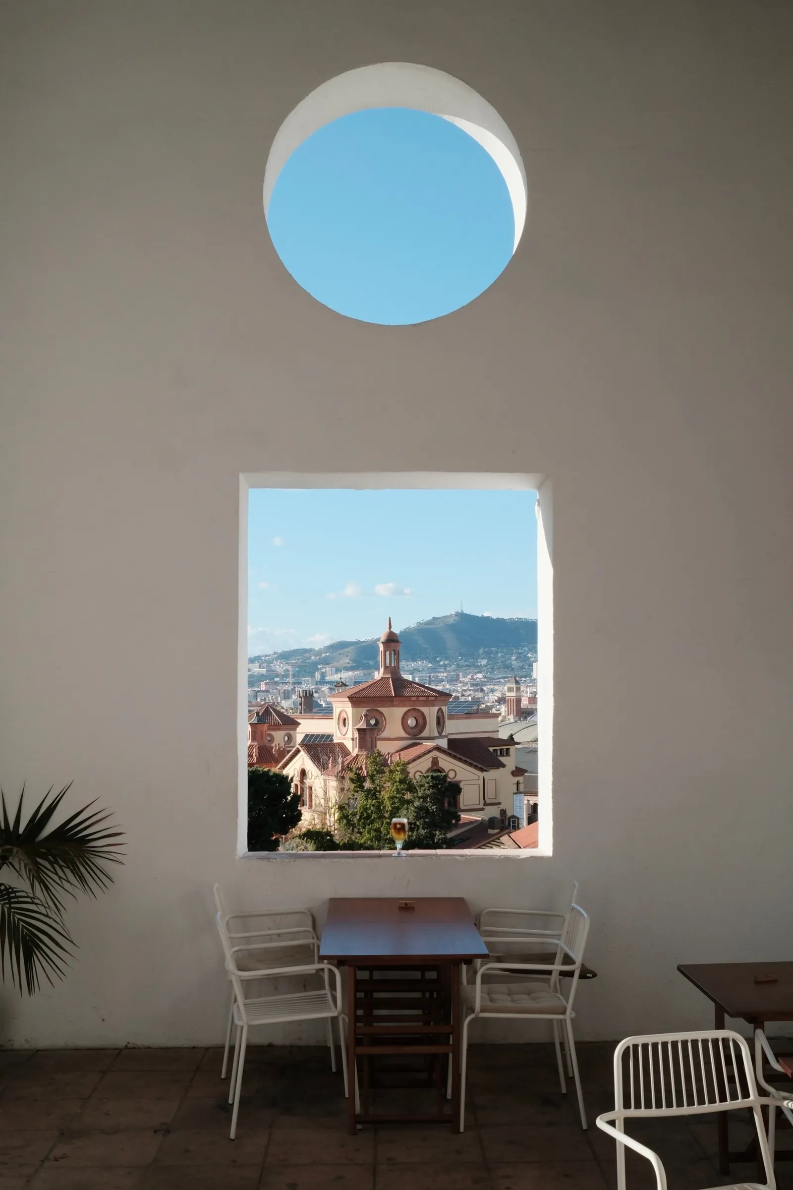 A whitewashed room with a round skylight and a window framing a church and hills