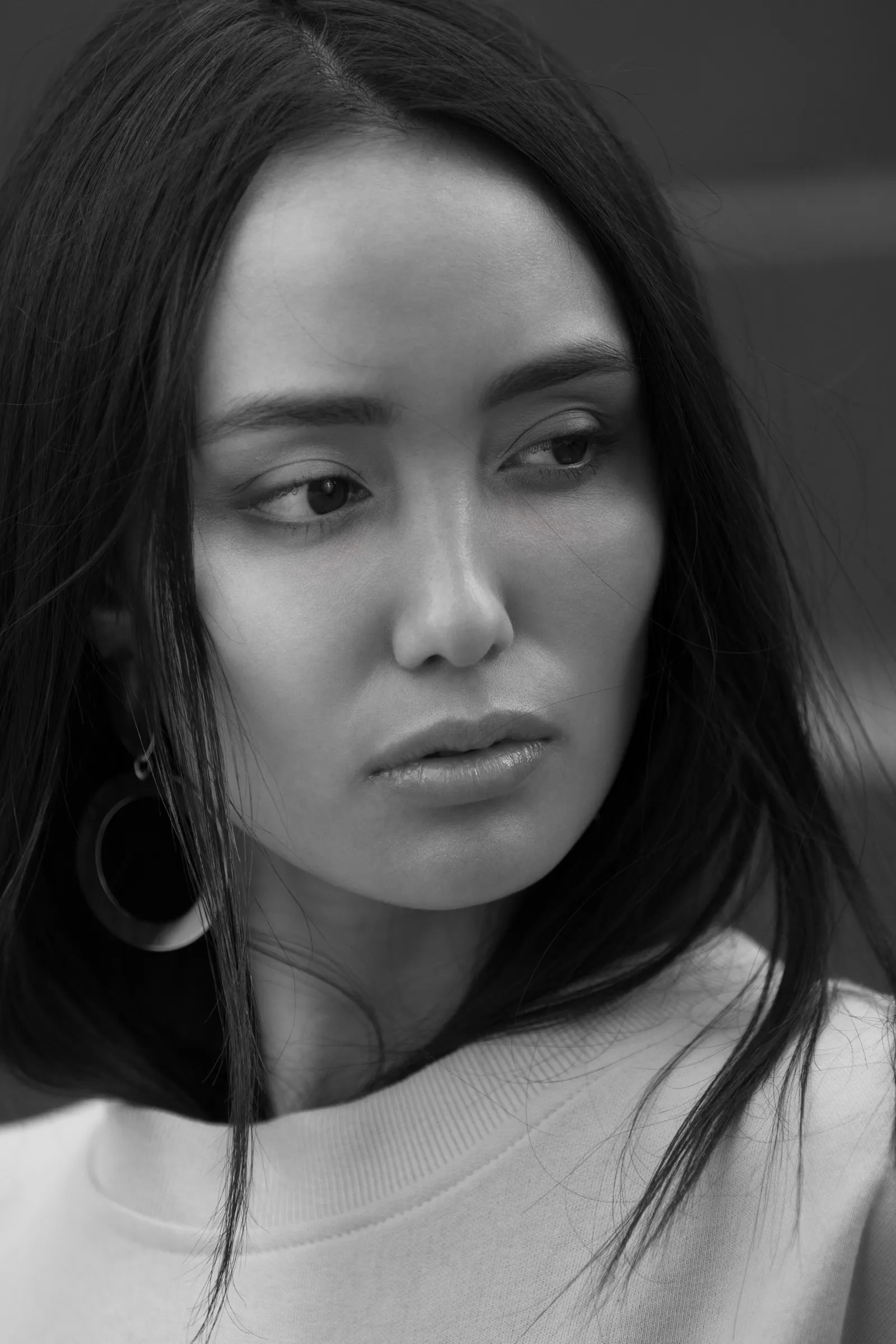 Black-and-white close portrait of a woman with long dark hair and a hoop earring, looking to the side