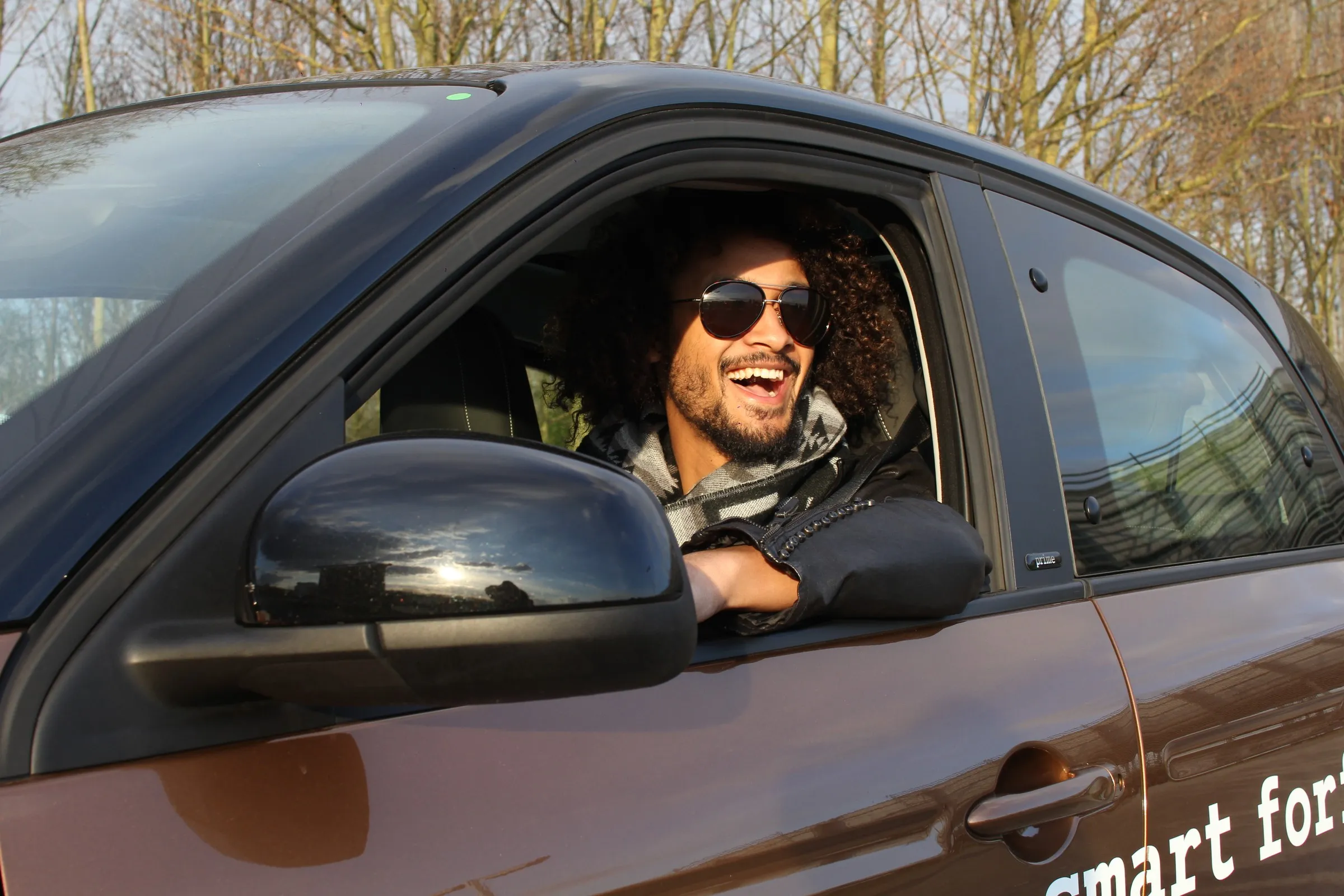A laughing man in sunglasses leaning out of the window of a dark car