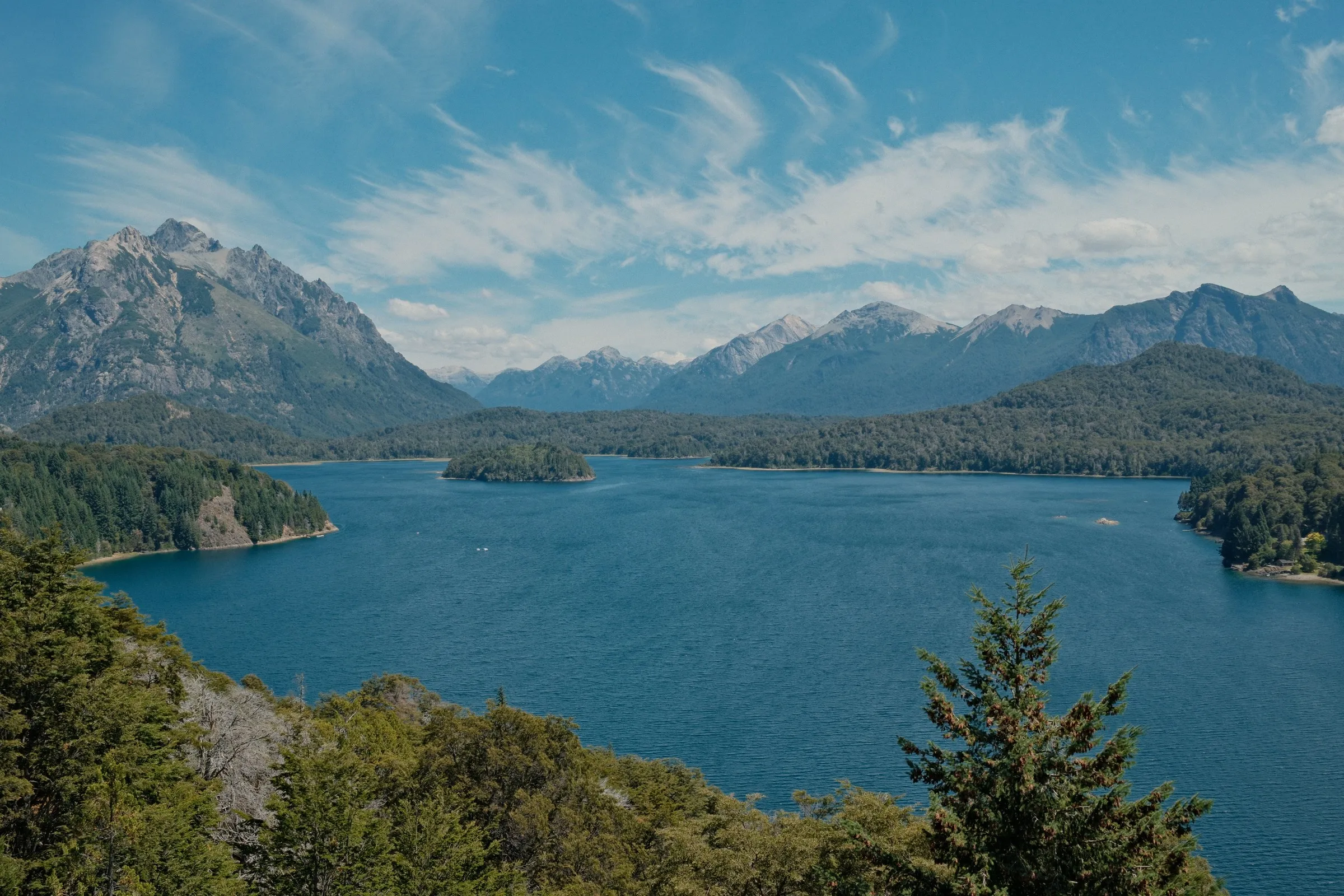 A deep blue lake surrounded by forested hills and mountains under a wide sky