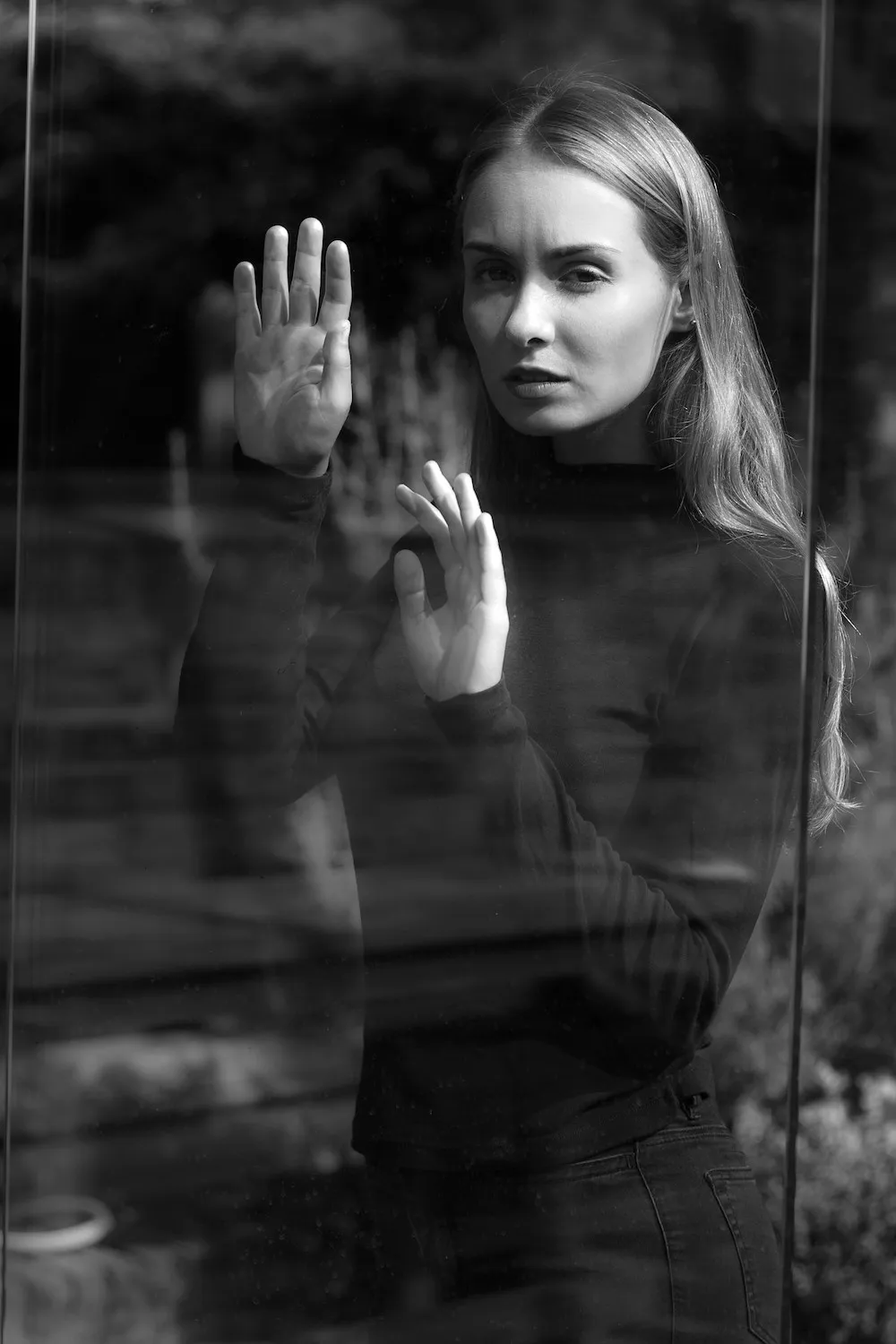Black-and-white portrait of a woman behind a glass pane, her hand pressed against it