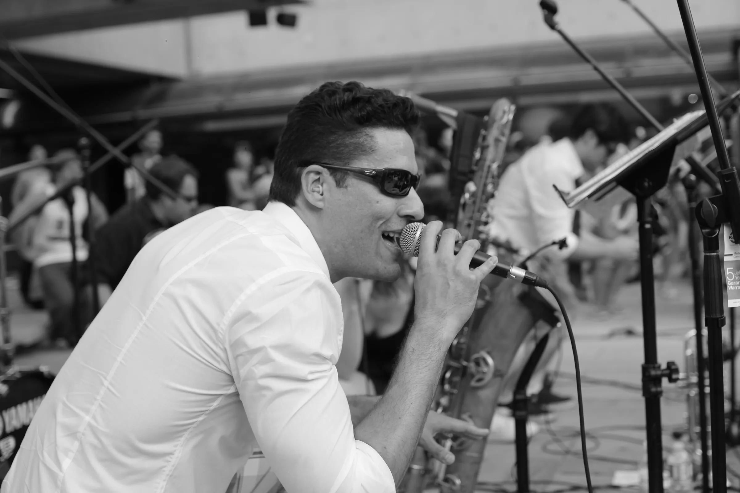 Black-and-white photo of a singer in sunglasses performing on stage next to a saxophone
