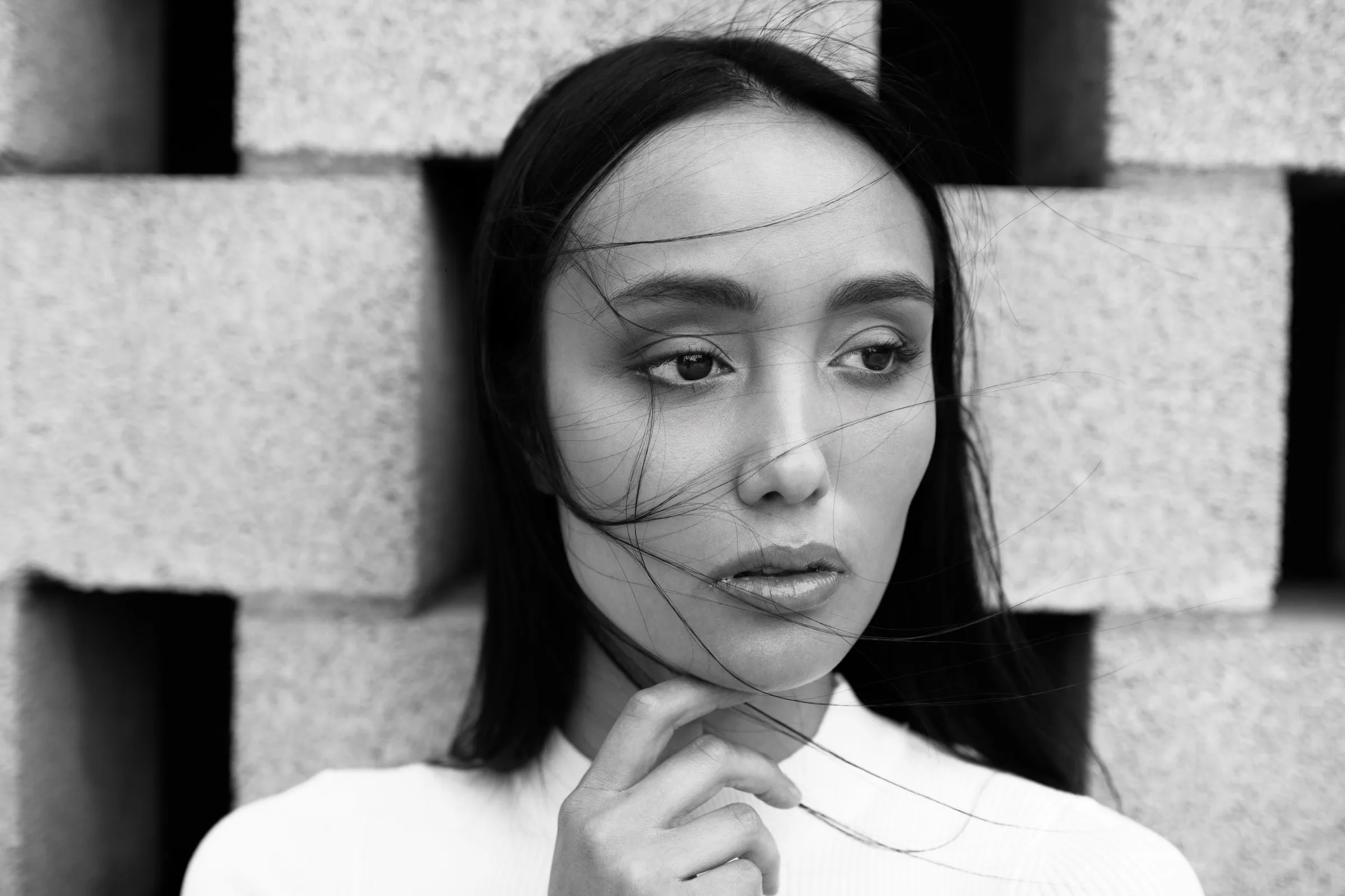 Black-and-white portrait of a woman with windswept hair in front of a concrete block wall