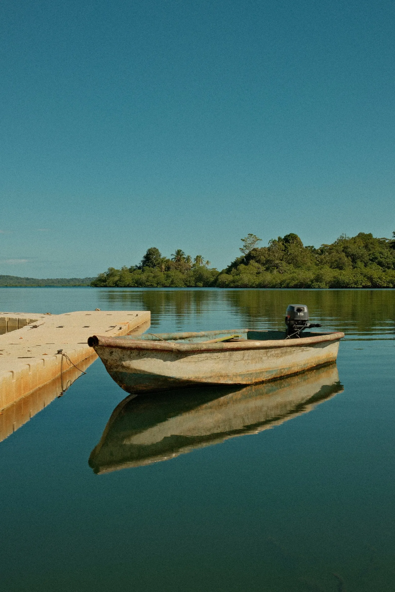 A wooden boat moored by a jetty on perfectly still water, with a green island behind