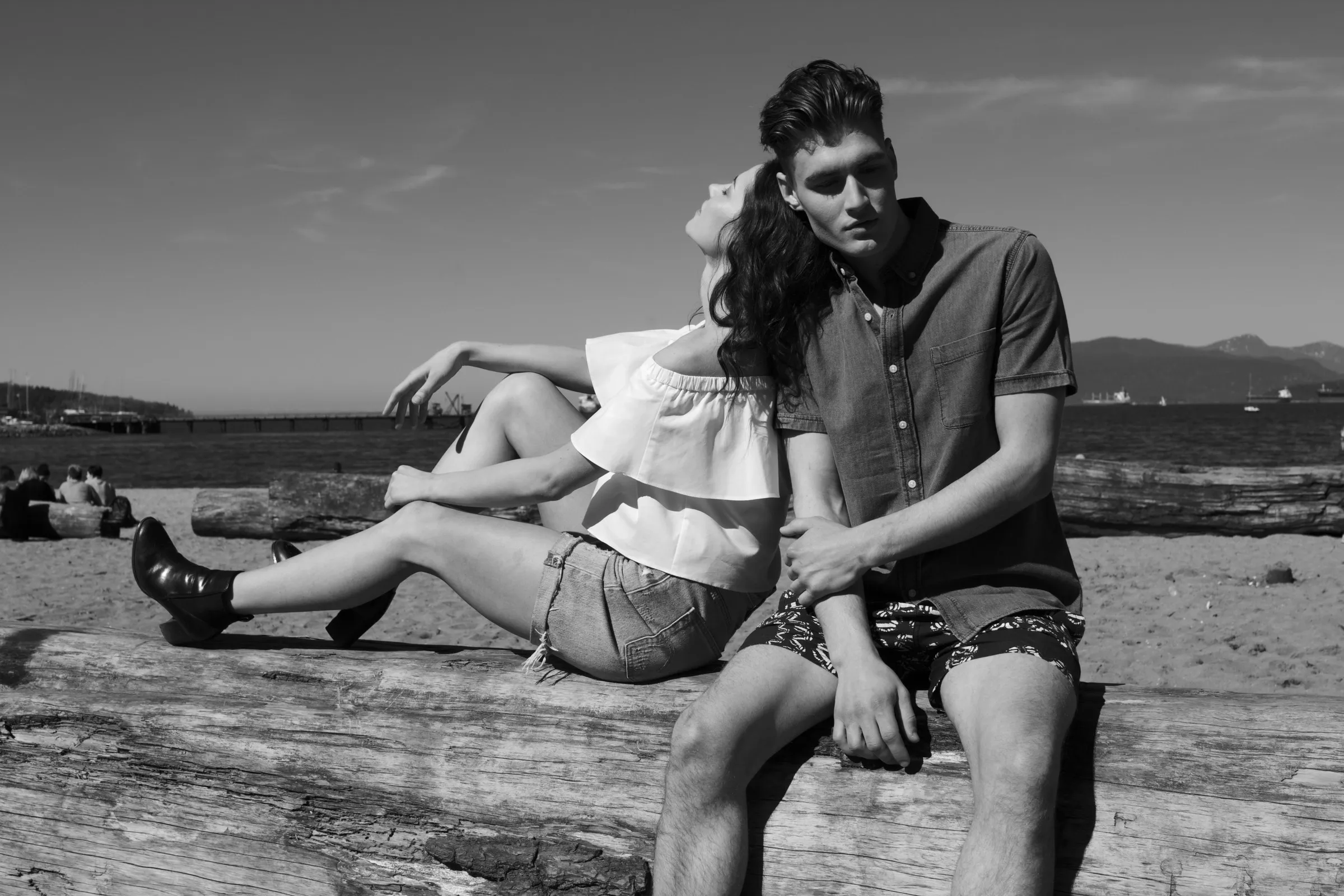 Black-and-white photo of a couple sitting on a driftwood log on a beach