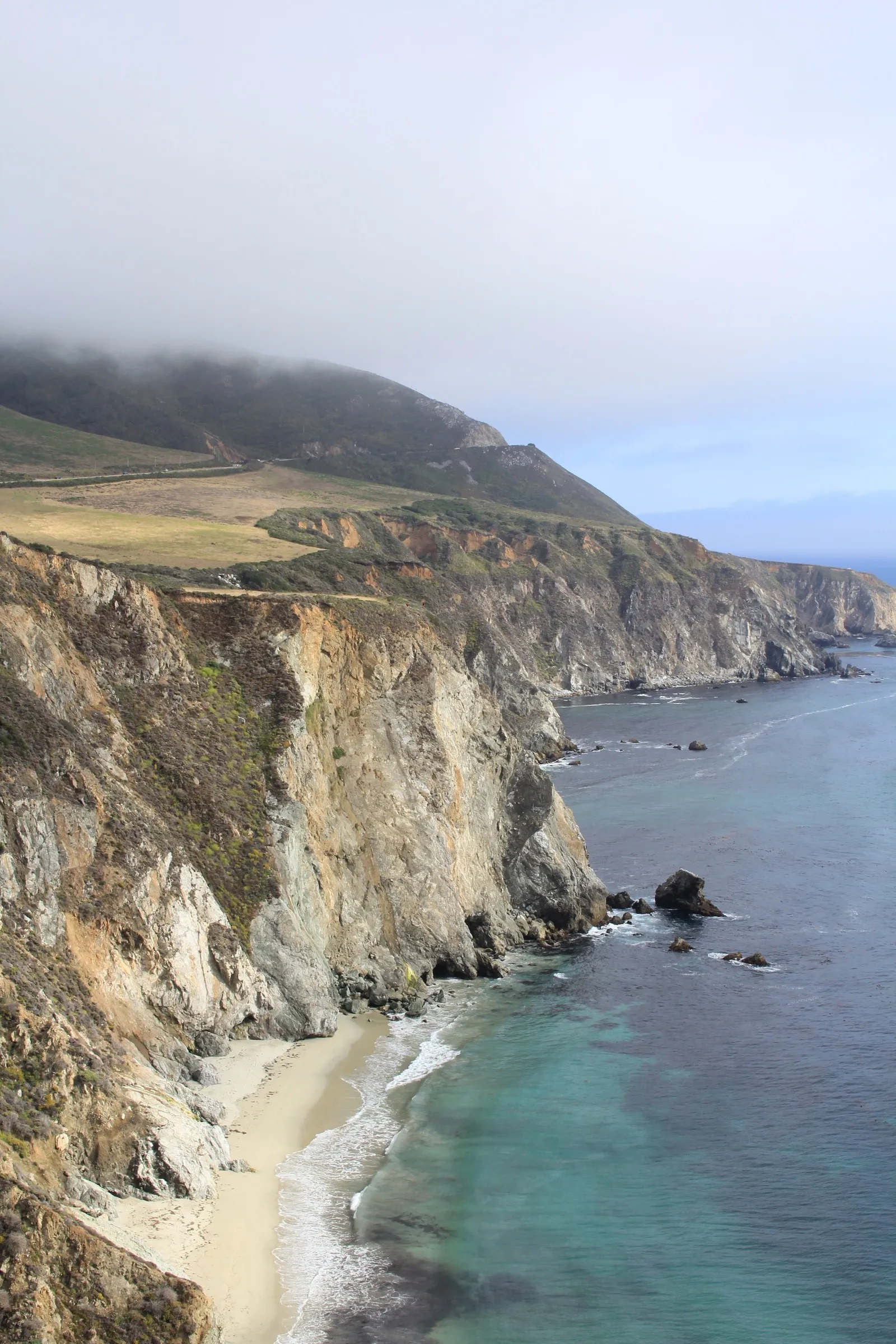 A rugged cliff coastline with a small beach under low clouds